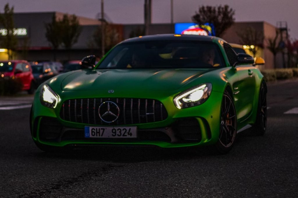 The image features a striking green sports car with its headlights on, parked in a lot at dusk.